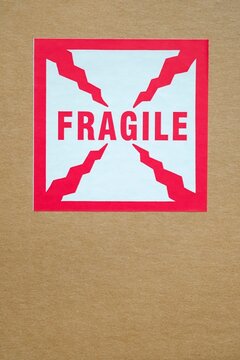 Close-up of a red and white "Fragile" sticker with crack-like graphic elements on a brown cardboard box - a clear caution for handling breakable contents during shipping and delivery.