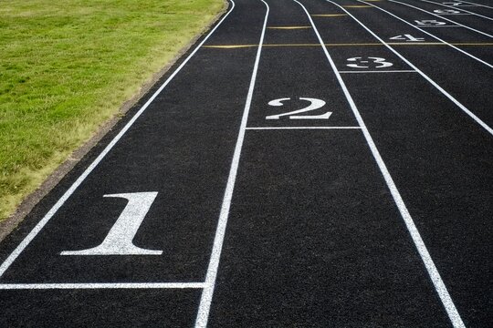 View of a black asphalt running track with white lane markings and numbers - a symbol of competition, fitness, and athletic training