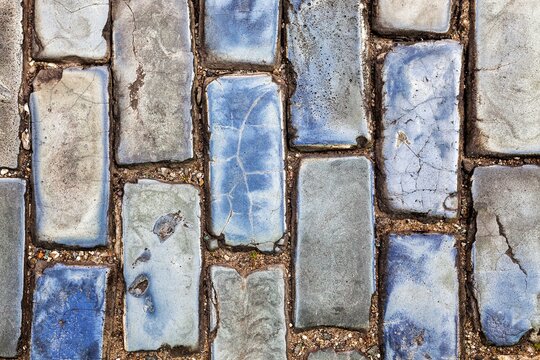 A close-up view of cracked blue cobblestones lining the historic streets of Old San Juan, blue glazed bricks or adoquines used as ballast for shipping in the colonial era. 