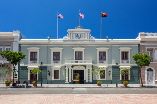 Front view of the Casa Alcaldia, the historic city hall building in Ponce, Puerto Rico, with flags flying under a clear blue sky and classic neoclassical architecture.