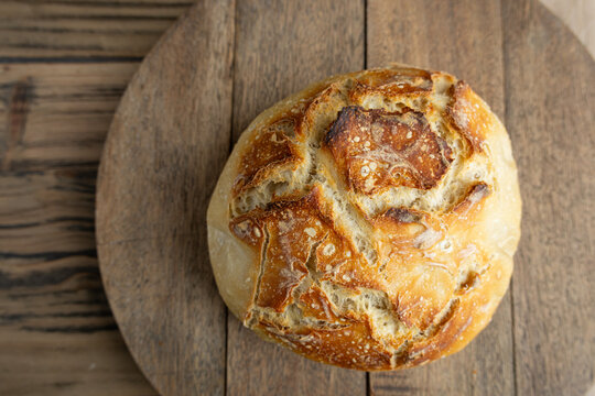 Rustic artisan sourdough bread loaf on wooden board, top view