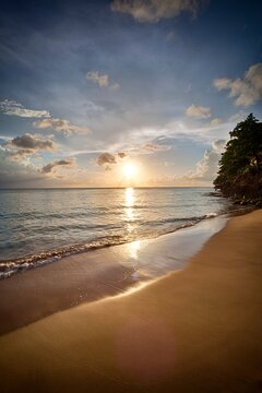 Golden light reflects on the smooth shoreline at Crash Boat Beach in Puerto Rico as the sun sets over the horizon. 
