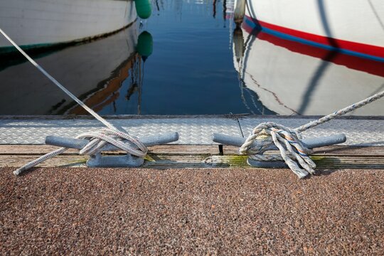 Nautical scene showing two boats moored with ropes secured to dock cleats at Charleston Marina in Oregon. The calm water reflects the hulls and dock equipment.