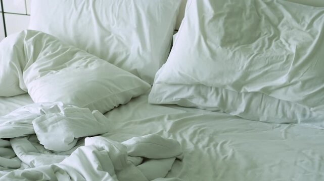 Unmade bed with wrinkled white linens and pillows in disarray, showcasing the progression of bedding arrangement from a top view perspective