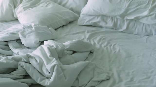 Unmade bed with wrinkled white linens and pillows, showcasing the gradual disarray of bedding from a top view perspective in a cozy bedroom setting