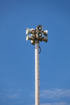 Tsunami warning system with multiple loudspeakers mounted on a tall wooden pole against a clear blue sky in Bandon, Oregon.