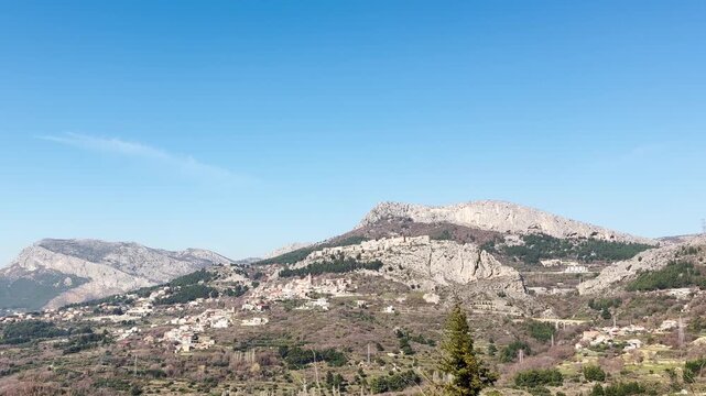 Close-up side view of Klis Fortress filmed from a moving car, showing the historic stone walls and hillside setting above the Split suburb under a clear blue sky.