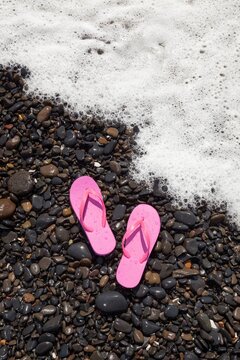 A pair of pink flip flops rest on wet rocks as a foamy ocean wave approaches the shore in Florence, Oregon.