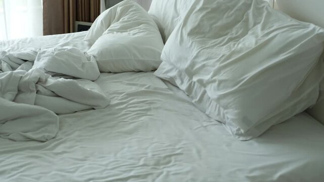 Unmade bed with rumpled white sheets and pillows, showcasing the gradual disarray of bedding in a bright, sunlit bedroom setting