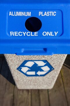 Outdoor recycling bin with blue lid labeled for aluminum and plastic, featuring a recycle symbol on the front.