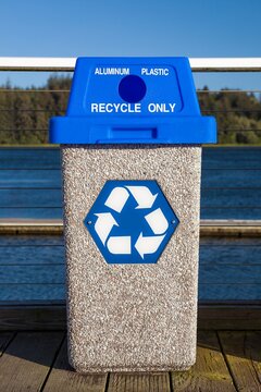 Public recycling bin with blue lid labeled for aluminum and plastic, featuring the classic three-arrow recycle symbol. Located in Florence, Oregon.