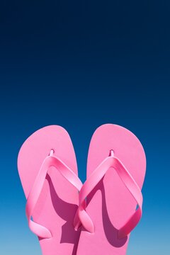 Close-up of bright pink flip flops held up against a vivid blue sky on a sunny day.
