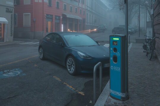 Tesla Model 3 electric vehicle charging on an A2A station in a Milan city street on a foggy day