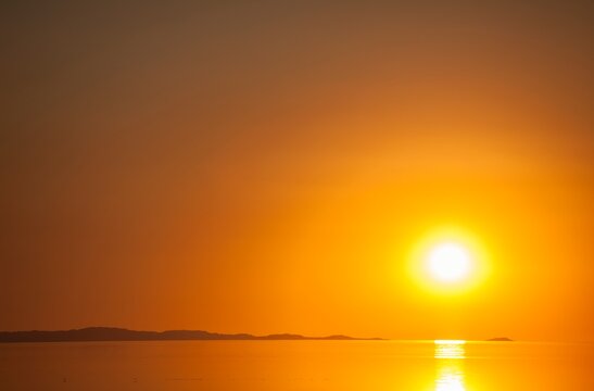 A fiery orange sun sets over the calm surface of the Great Salt Lake, casting golden reflections across the water.