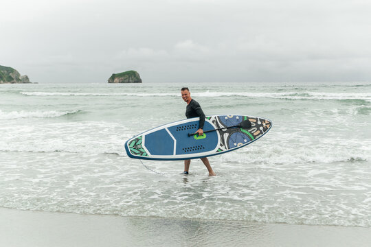 Man carrying paddleboard out of the sea.