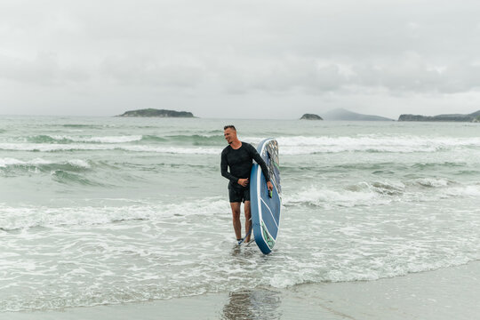 Smiling man with sup board standing in ocean waves.