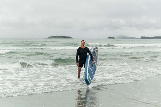 Happy surfer laughing with sup board on a cloudy beach.