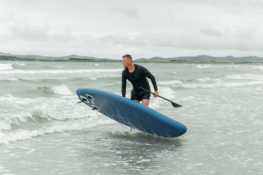 Man carrying paddleboard out of the water.
