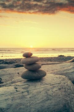 Smooth stones balanced on driftwood at Ruby Beach, Olympic Peninsula, Washington, with the sun setting over the Pacific Ocean in warm golden light.
