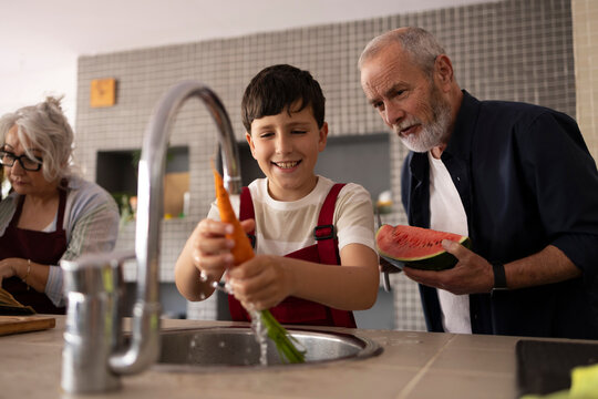 Grandson learning to cook with mother and grandparents in kitchen
