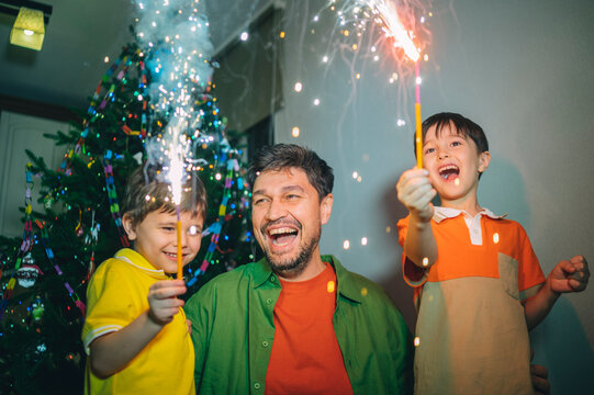 Parent and children celebrating birthday with sparklers by festive tree
