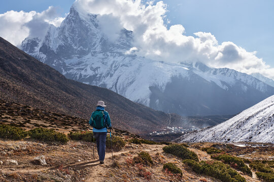 Happy female trekker with backpack walks on mountain path towards Dingboche village, surrounded by snow-capped Himalayan peaks during Everest Base Camp trek, Nepal.