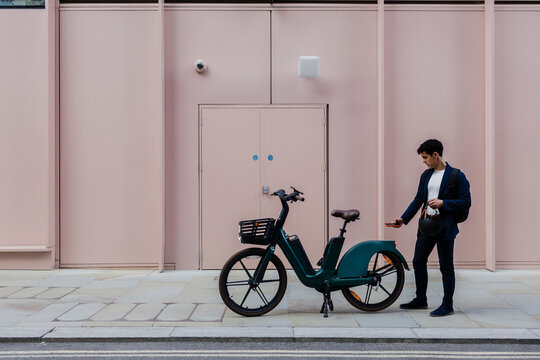 Businessman using smartphone app for electric bike sharing outdoors