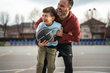 Fototapeta premium Father and son laughing playing basketball outdoors