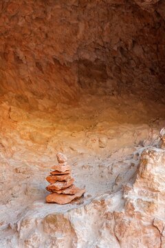 A balanced stack of red and orange sandstone rocks forms a small cairn in Bryce Canyon National Park, set against a sunlit backdrop of textured canyon walls.
