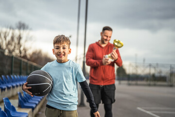 Young boy holding basketball with proud father celebrating trophy