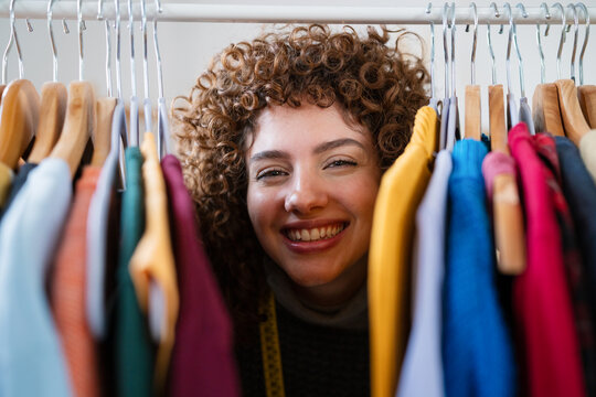 Smiling creative designer browsing clothes on rack indoors