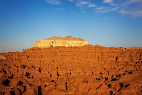 Expansive view of countless hoodoo rock formations under warm evening light, with a striking white mesa rising in the distance at Goblin Valley State Park, Utah.