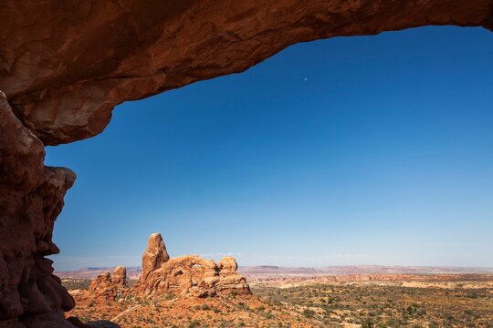 Scenic view of Turret Arch framed by the sandstone curve of North Window Arch in Arches National Park, Utah, with a vast desert landscape under a clear blue sky.