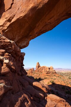 Scenic view of Turret Arch framed by the sandstone curve of North Window Arch in Arches National Park, Utah, with a vast desert landscape under a clear blue sky.