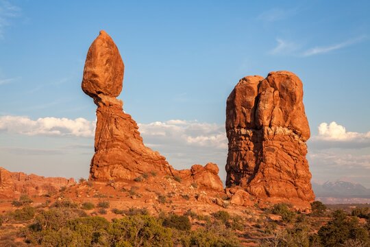 Balanced Rock glows in the warm light of sunset in Arches National Park, Utah, highlighting the striking contrast between the massive sandstone formation and the surrounding desert landscape.