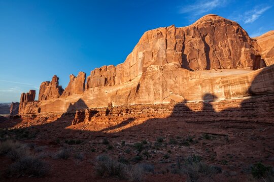 Golden evening light illuminates the towering sandstone cliffs of the Park Avenue rock formation in Arches National Park, Utah, casting dramatic shadows across the red desert landscape.