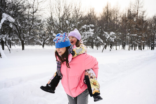 Mother giving piggyback ride in winter outdoors wearing warm clothes
