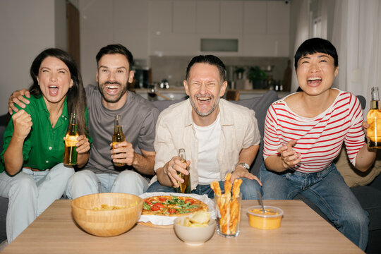 Friends enjoying football and snacks at home, laughing and celebrating