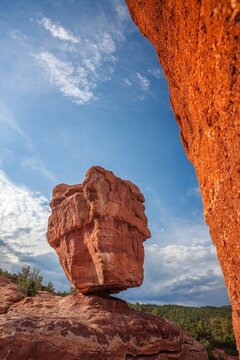 Balanced Rock rises from red sandstone in Garden of the Gods, Colorado Springs, framed by a nearby cliff and blue sky with late-day clouds.