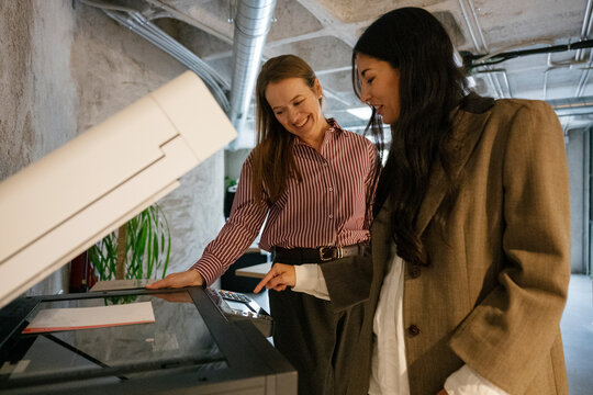 Colleagues using copy machine in modern office environment