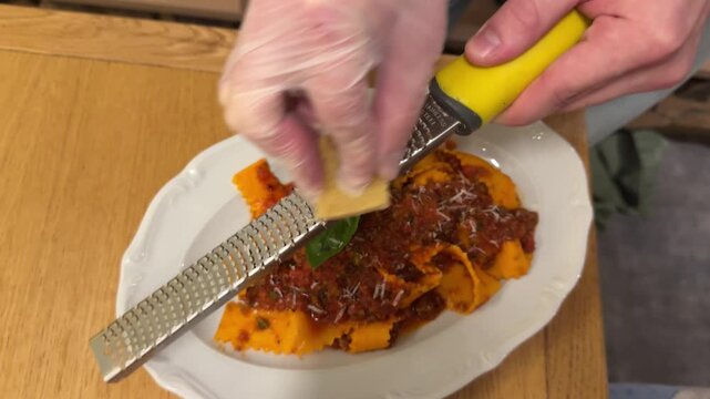 Waiter grates fresh Parmesan over pasta at an Italian restaurant table, fluffy cheese snowing onto steaming twirls amid savory aroma and candlelight.