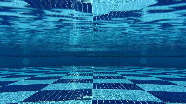 Underwater camera captures mesmerizing sunlight patterns in the pool, with rays creating shimmering caustics and ripples dancing across the tiled bottom.