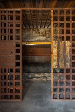 Interior of an antique frontier jail cell with rusty iron bars, an open door, padlock, and narrow bunk