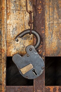 Close view of a vintage padlock and chain hanging on a rusty jail door, with iron bars and weathered paint