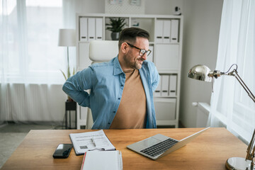 Man suffering from back pain working at office desk