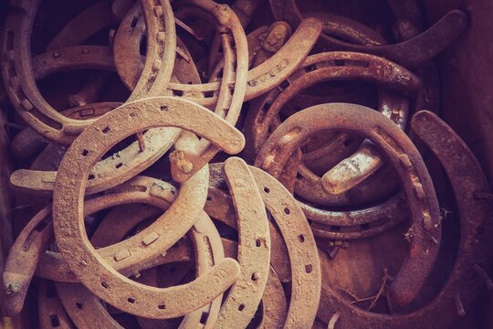 Close view of a pile of old rusty horseshoes in a barn, showing weathered metal, patina, and gritty texture.