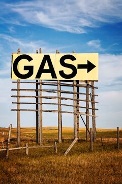Large roadside GAS arrow sign on a weathered wooden billboard stands in a rural prairie under a blue sky, suggesting fuel ahead, travel, and open road vibes in the Great Plains, South Dakota