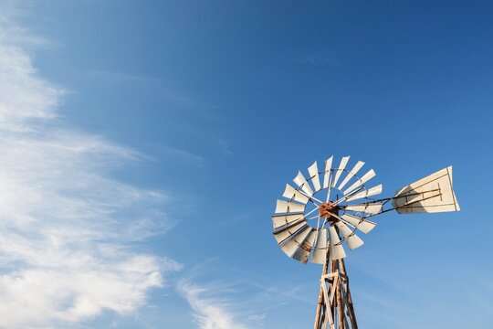 An old prairie windmill rises against a wide blue sky in South Dakota, thin clouds drifting past and plenty of open space for text, a rustic symbol of ranch life on the Great Plains.