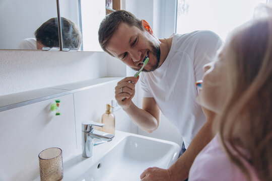 Father and daughter brushing teeth together in bathroom morning routine
