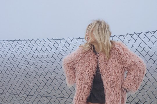 Fashion portrait with fur coat and messy hair outdoors at fence